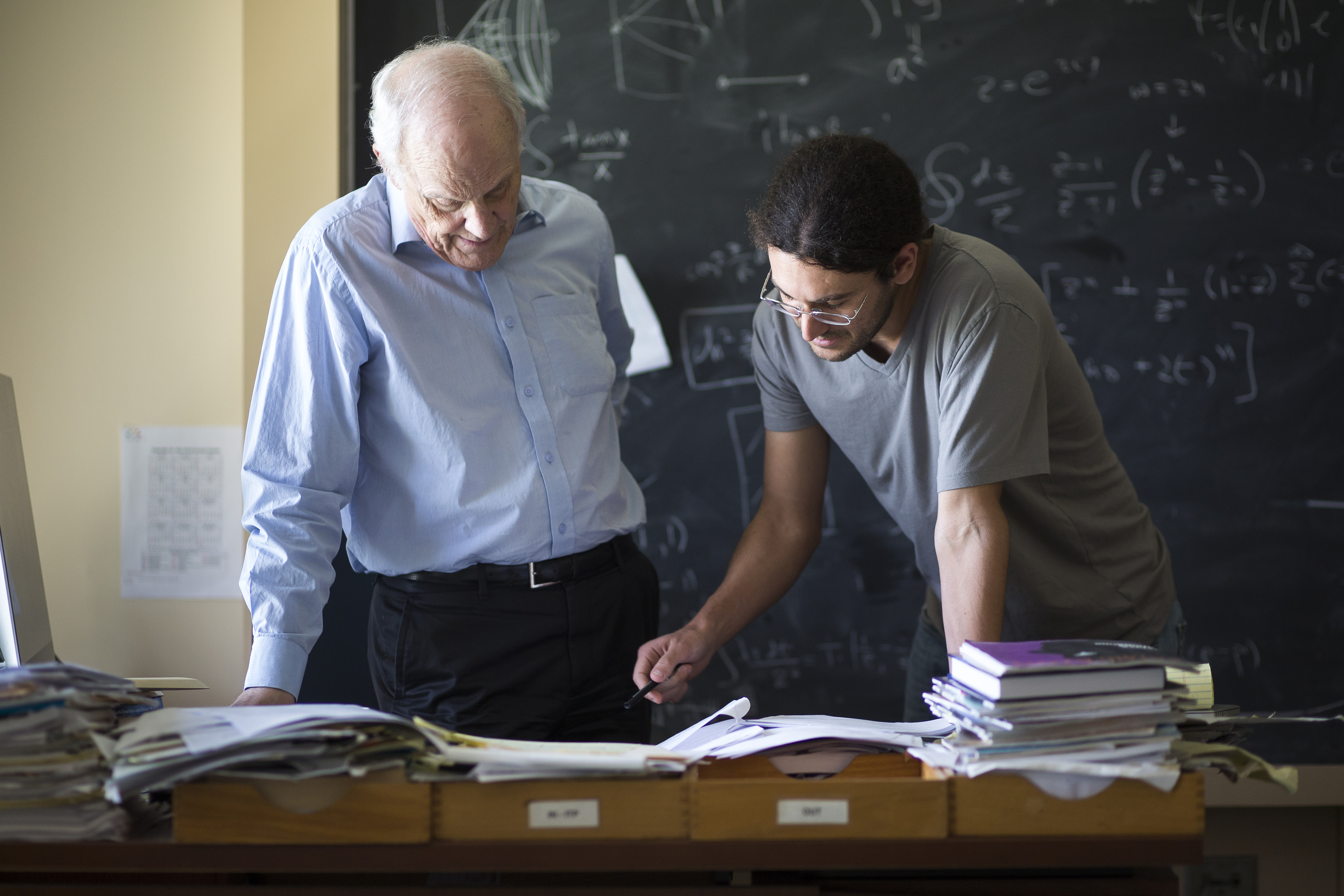 A student asking their professor a question, overlooking a question on a notebook